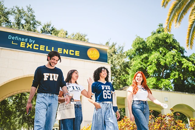 FIU students walk under a sign reading, "Defined by Excellence"